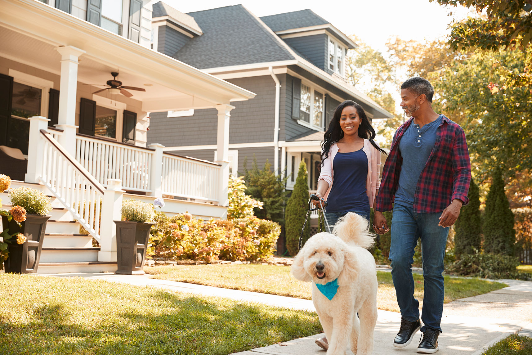 an African-American couple walking a white labradoodle through a Circle East District residential neighborhood