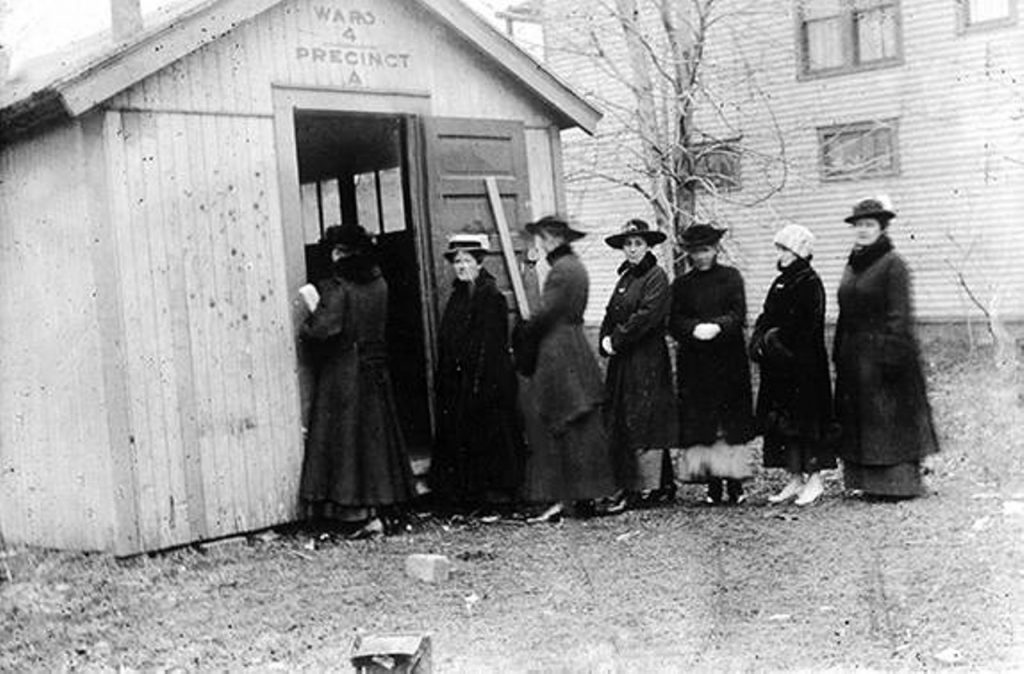 History of East Cleveland: 1916 Women's Suffrage | Historic photo showing a line of women waiting to vote outside a white wood-clapboard shack identified as Ward 4, Precinct 4
